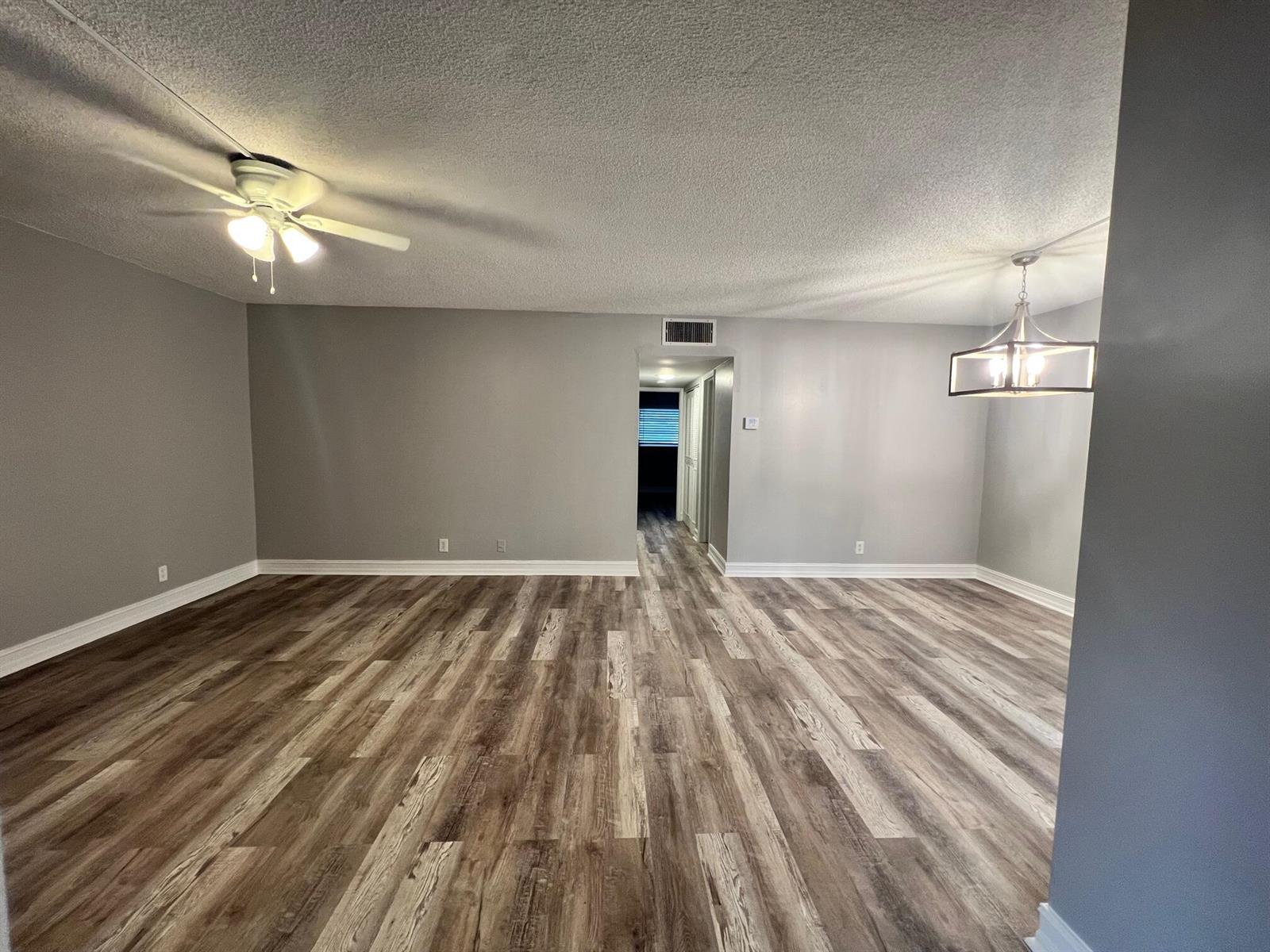 An empty room features gray walls, wood-look flooring, a ceiling fan, and a hanging light fixture — 1340 NE 28th Avenue # 243, Pompano Beach FL 33062, POMPANO BEACH, FL
