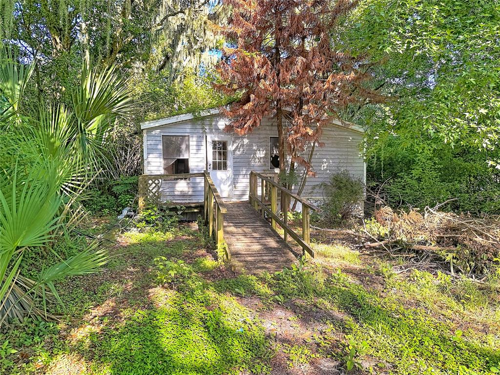 A small, weathered house with a wooden ramp entrance sits surrounded by overgrown trees — 8216 SIMPSON LANE, LAKELAND, FL