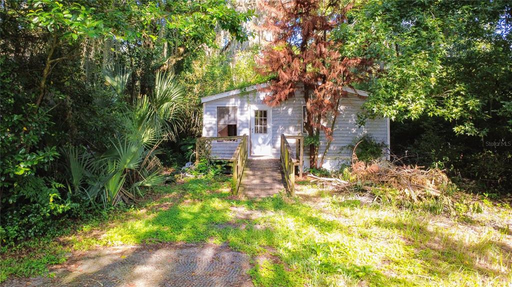 A small, weathered light-gray house sits nestled among dense trees and overgrown vegetation — 8216 SIMPSON LANE, LAKELAND, FL