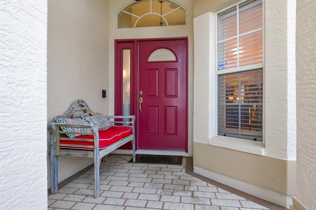 A front entryway features a magenta door, a wooden bench with red cushions, and pavers — 11328 HOLLANDER AVENUE, HUDSON, FL