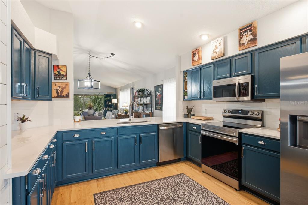 A kitchen with blue cabinets, stainless steel appliances, white countertops, and light wood flooring — 11328 HOLLANDER AVENUE, HUDSON, FL