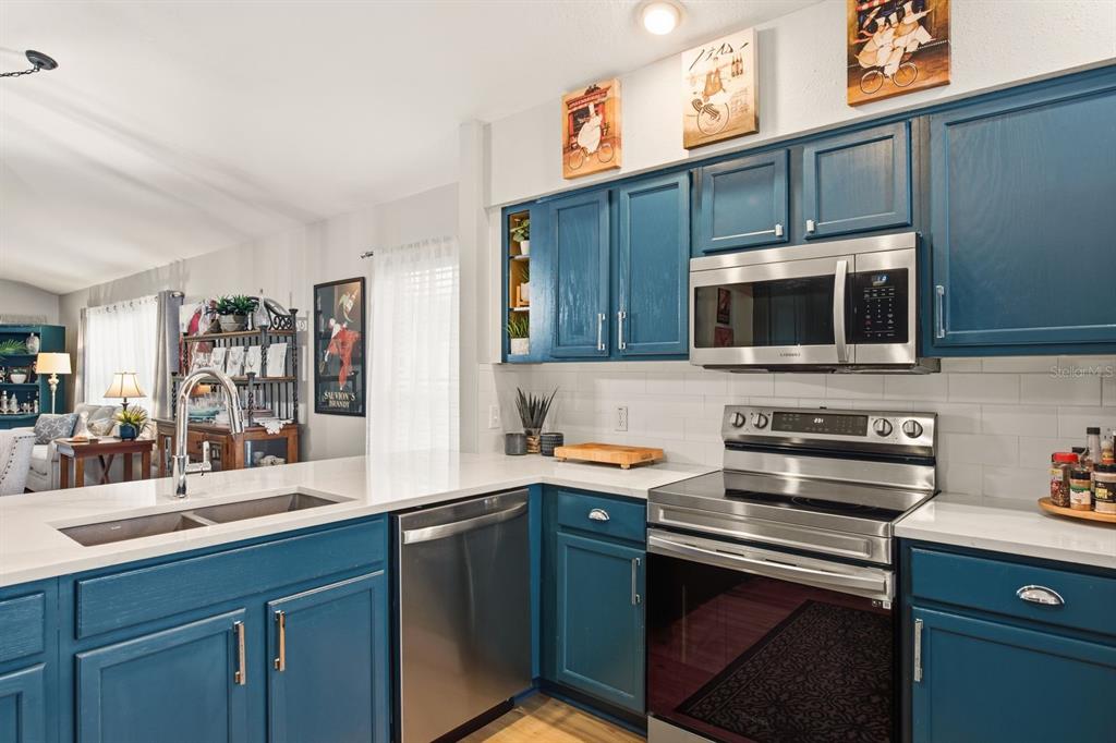 A kitchen features blue cabinets, stainless steel appliances, white countertops, and a subway tile backsplash — 11328 HOLLANDER AVENUE, HUDSON, FL