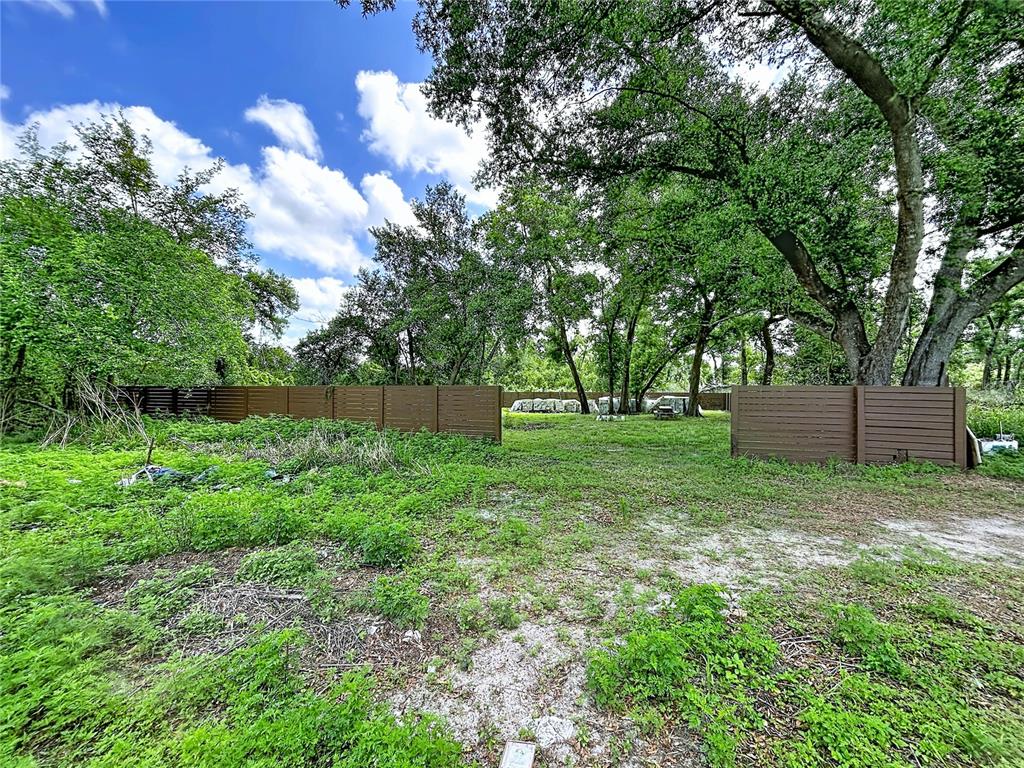 A grassy, partially cleared lot features a brown horizontal-slat fence and mature trees — 1029 ROBSON AVENUE, SEFFNER, FL