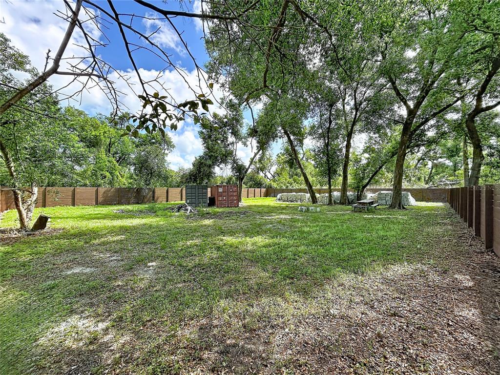 A grassy backyard features mature trees, a wooden fence, and two shipping containers — 1029 ROBSON AVENUE, SEFFNER, FL
