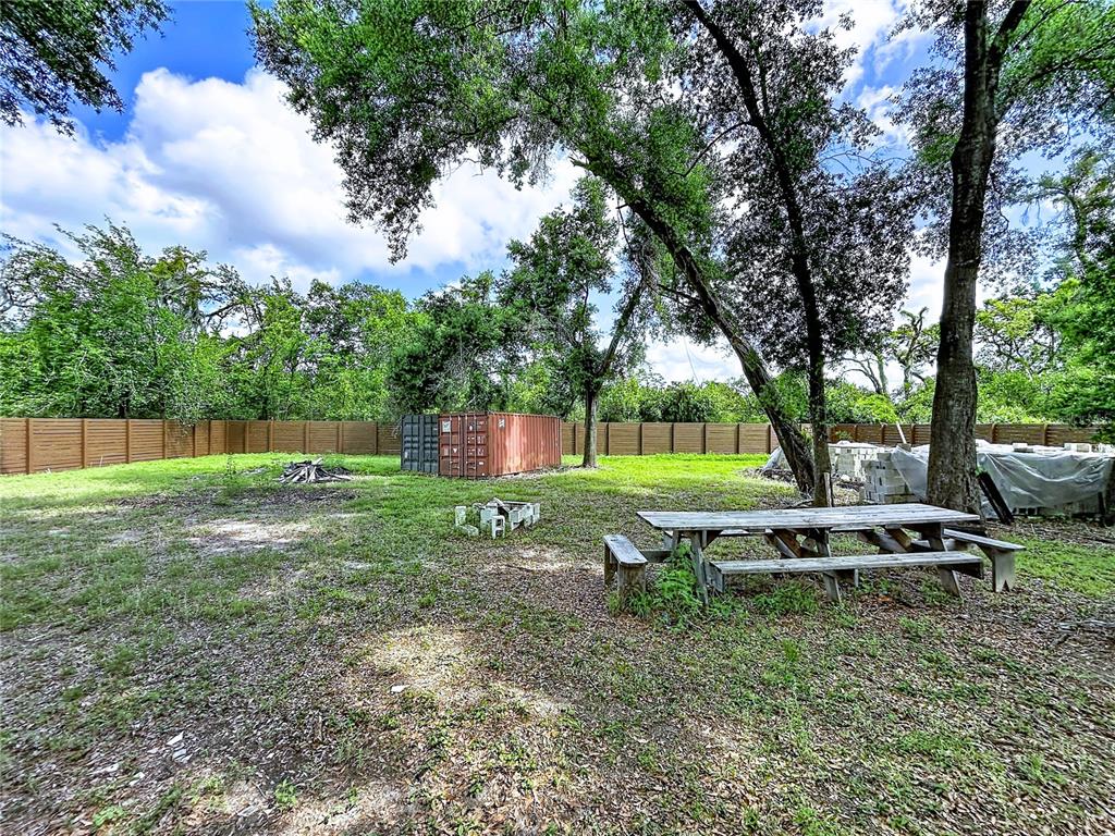 A backyard features a wooden picnic table, a shipping container, and a tall privacy fence — 1029 ROBSON AVENUE, SEFFNER, FL