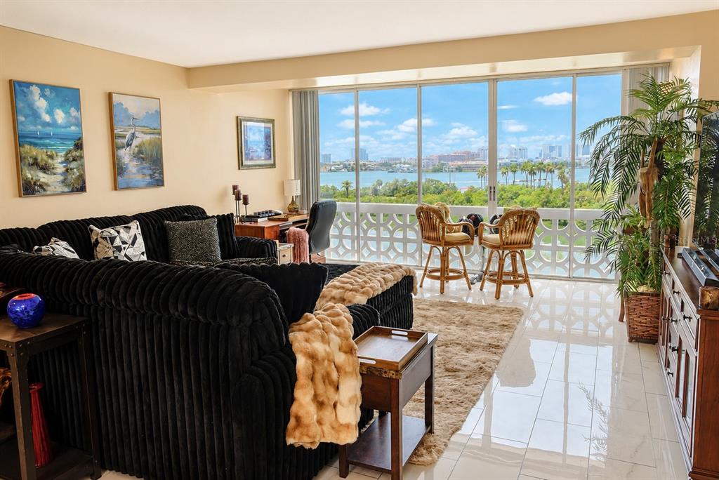 A living room with a black sectional sofa, tiled floors, and a balcony overlooking water — 31 ISLAND WAY UNIT 505, CLEARWATER BEACH, FL