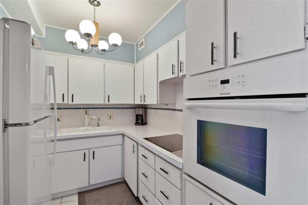 A white kitchen features white cabinets, a wall oven, a sink, and a light fixture — 31 ISLAND WAY UNIT 505, CLEARWATER BEACH, FL