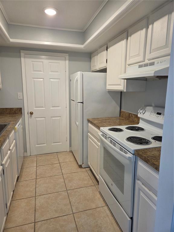 A galley kitchen features white cabinets, white appliances, tan countertops, and light-colored tile flooring — 743 E ALFRED STREET, TAVARES, FL