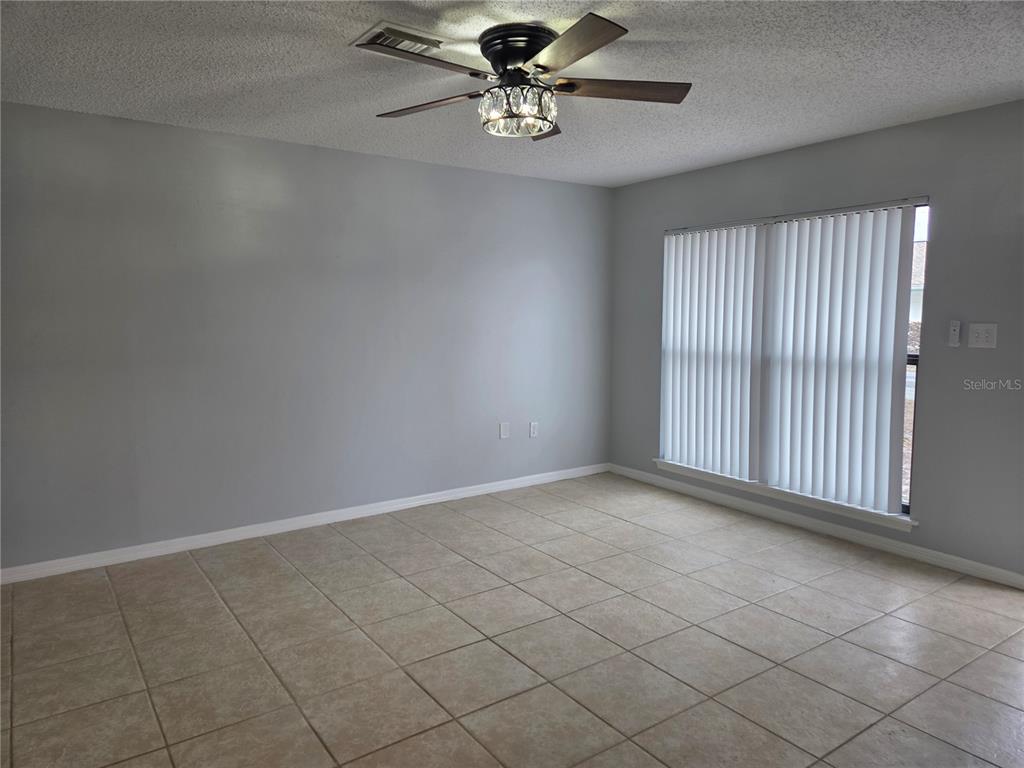 An empty room features light gray walls, beige tile flooring, and a crystal ceiling fan — 743 E ALFRED STREET, TAVARES, FL