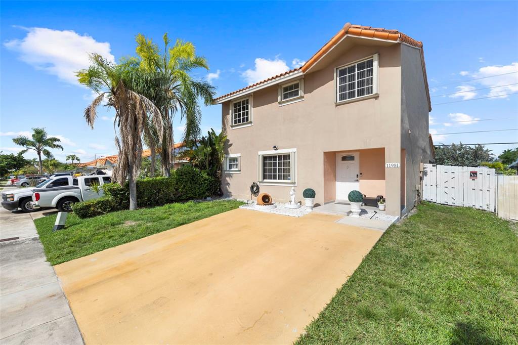 A two-story house with a tan stucco exterior, a concrete driveway, and a palm tree — 11951 SW 208TH TERRACE, MIAMI, FL