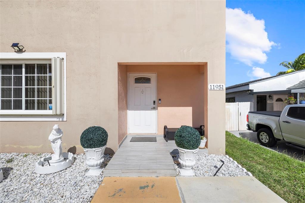 The exterior of a house features a white front door, tiled entryway, and decorative planters — 11951 SW 208TH TERRACE, MIAMI, FL
