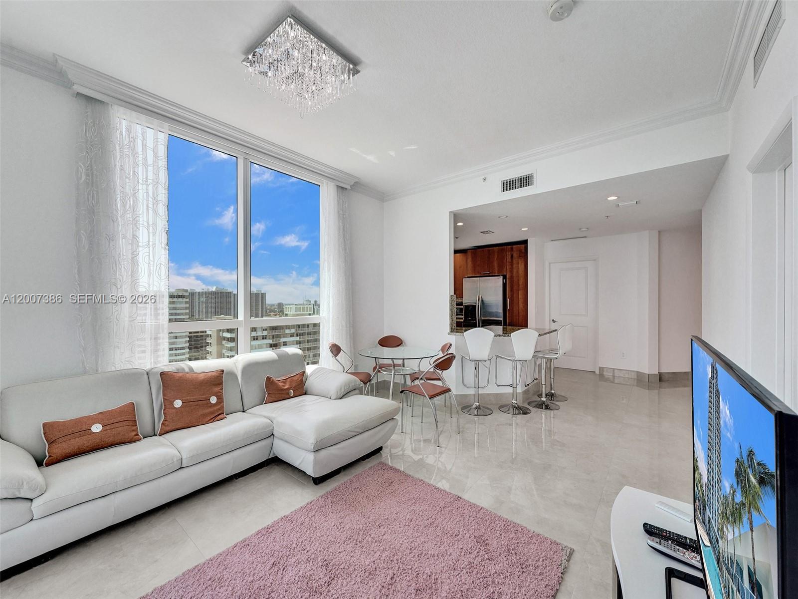 A modern living room features a white sectional sofa, a pink rug, and a kitchen area — 1945 S Ocean Dr # 2101, Hallandale Beach FL 33009, HALLANDALE BEACH, FL