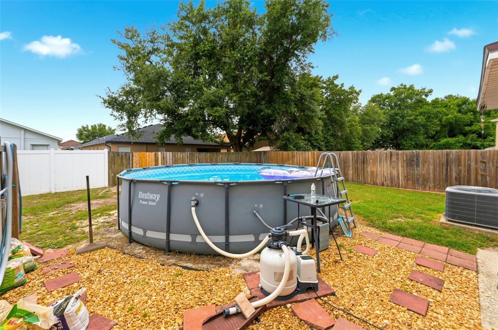 A backyard features an above-ground swimming pool with a pump system and a wooden fence — 1832 HOLTON ROAD, LAKELAND, FL