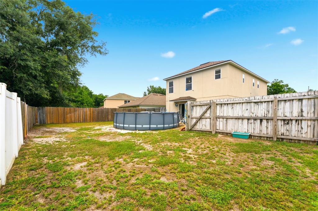 A backyard features a patch of grass, a circular above-ground pool, and a wooden fence — 1832 HOLTON ROAD, LAKELAND, FL