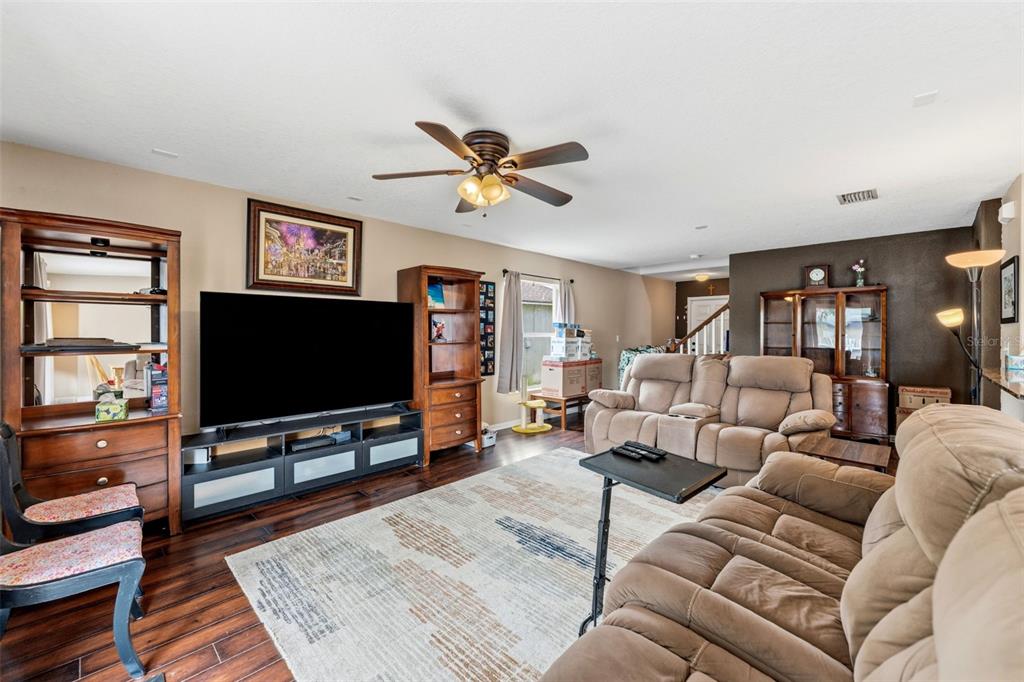 A living room features a large television, wooden shelving, beige reclining sofas, and hardwood floors — 1832 HOLTON ROAD, LAKELAND, FL
