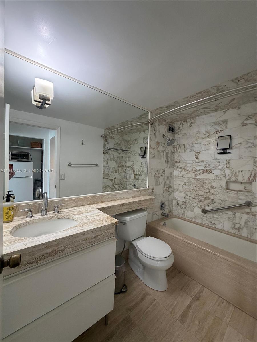 A bathroom features a marble-tiled tub surround, a vanity with a stone countertop, and a mirror — 700 Biltmore Way # 1216, Coral Gables FL 33134, CORAL GABLES, FL