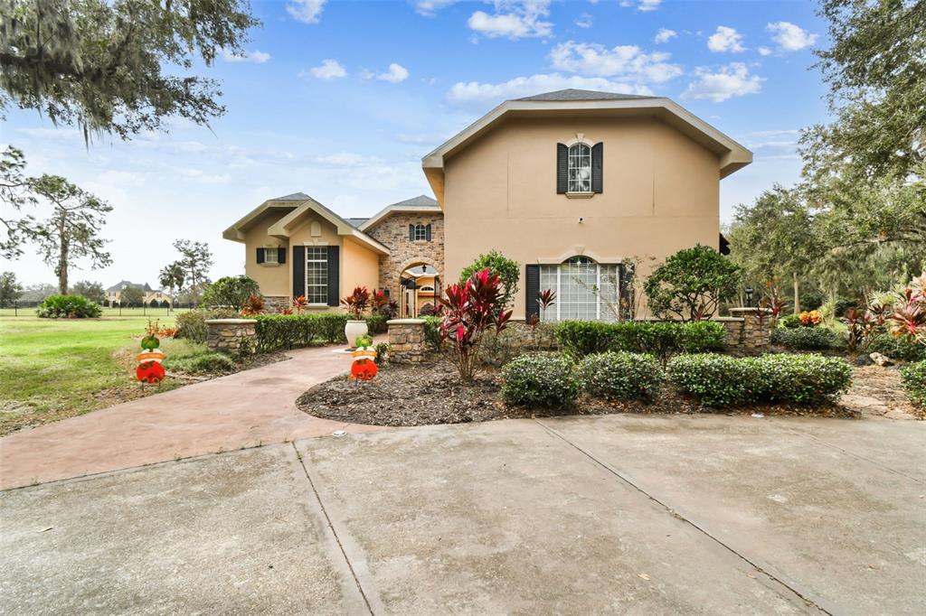 A two-story tan house with a stone entryway and a concrete driveway — 12709 MANNHURST OAK LANE, LITHIA, FL