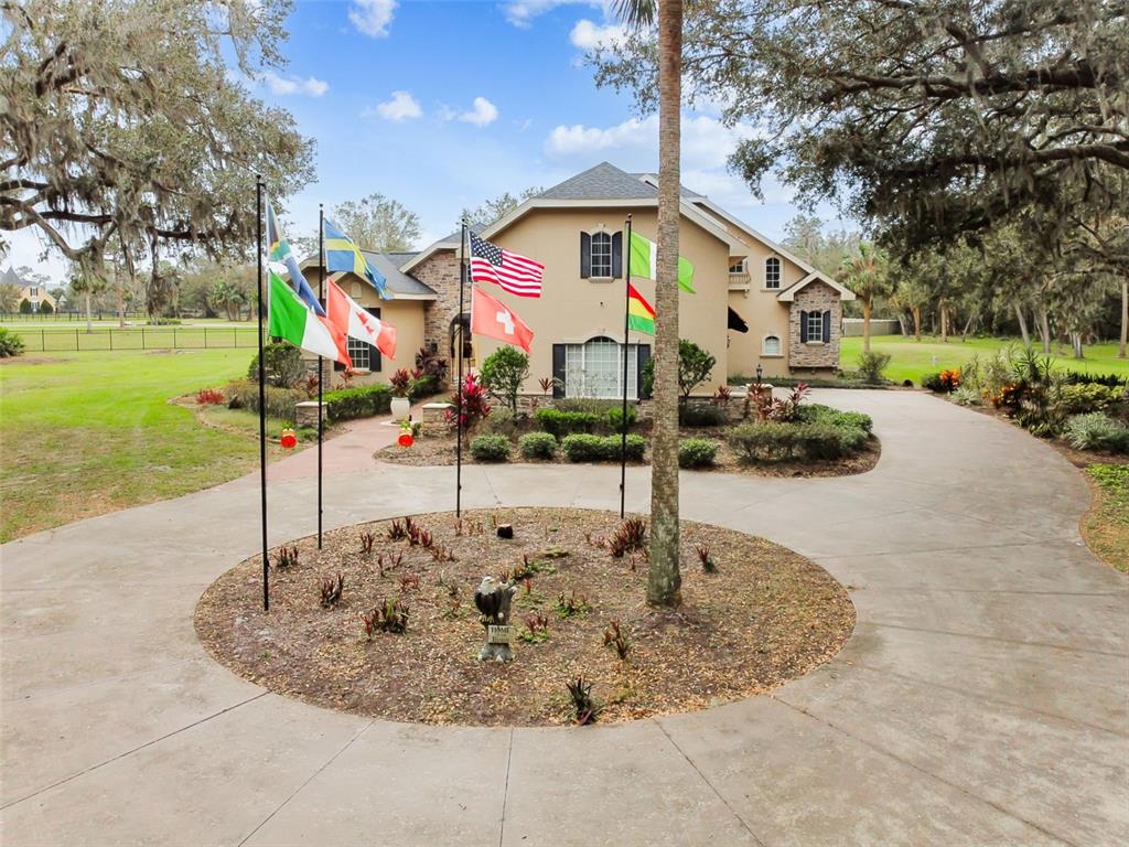 A large house with a circular driveway and several flagpoles in the front yard — 12709 MANNHURST OAK LANE, LITHIA, FL
