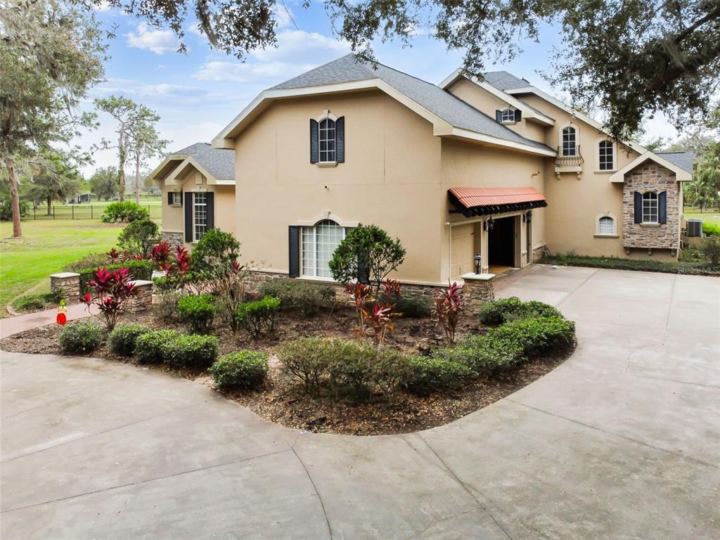 A two-story house with a beige stucco exterior, stone accents, and a large concrete driveway — 12709 MANNHURST OAK LANE, LITHIA, FL