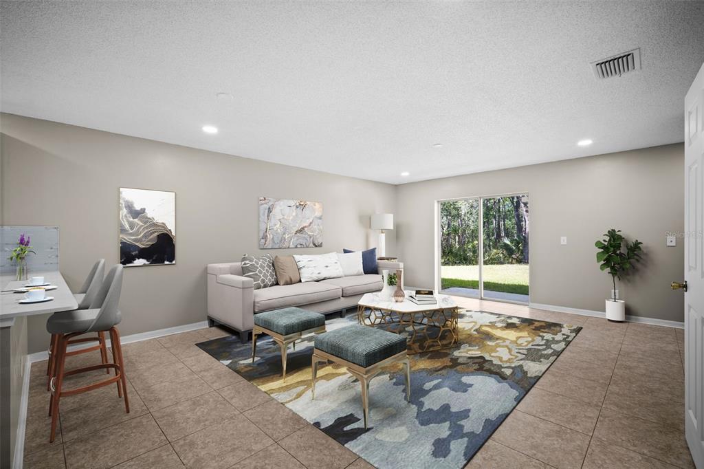 A living room features tile flooring, a sofa, two ottomans, a rug, and sliding glass doors — 4535 WINDING RIVER WAY, LAND O LAKES, FL