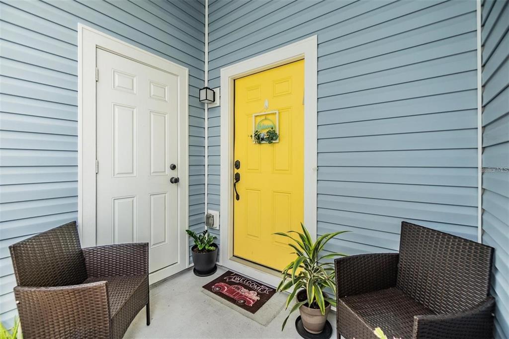 A porch features a yellow front door, a white side door, and two wicker chairs — 1265 JADE PLACE, CLEARWATER, FL