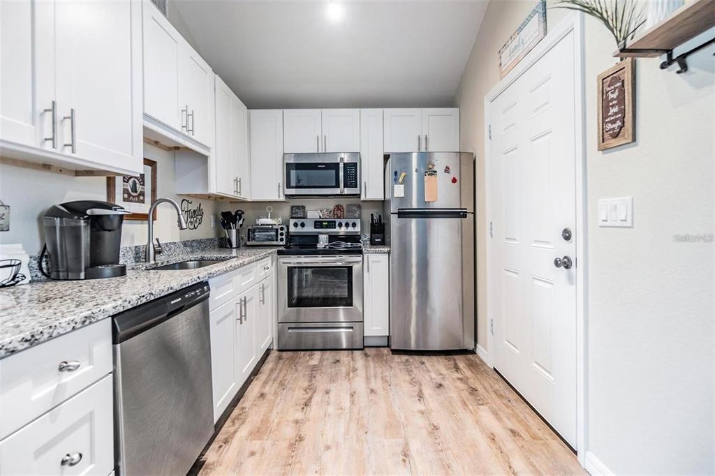 A kitchen features white cabinets, stainless steel appliances, granite countertops, and wood-look flooring — 1265 JADE PLACE, CLEARWATER, FL