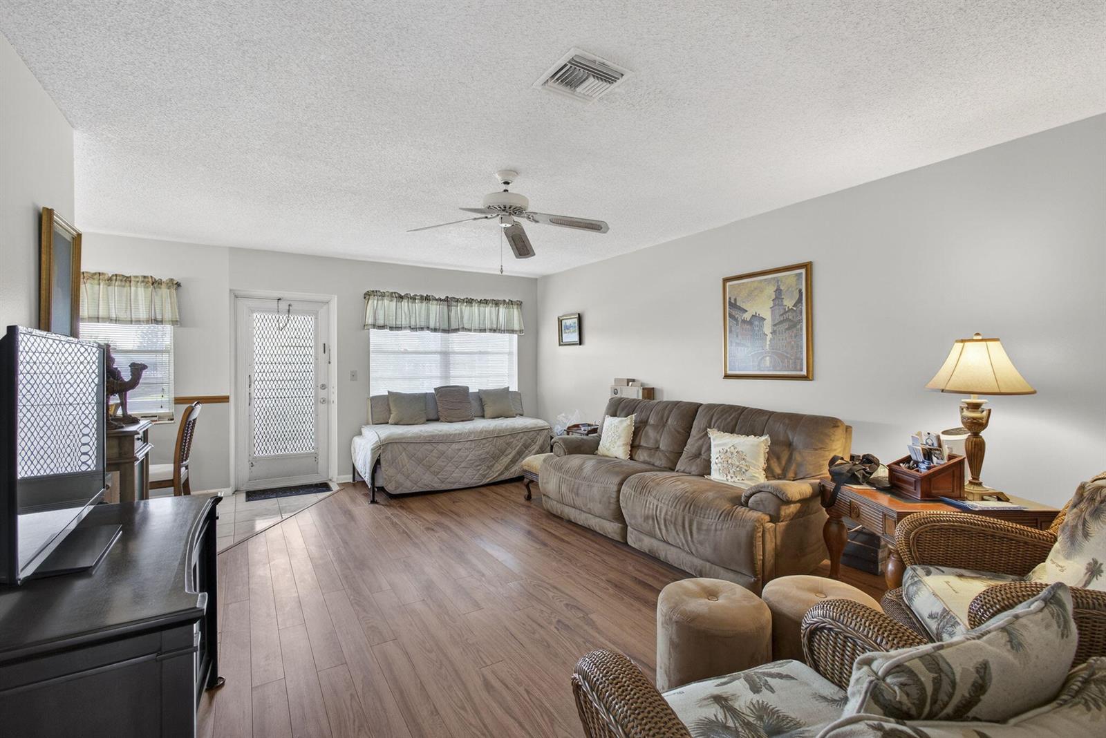 A living room features wood-look flooring, a ceiling fan, a sofa, and a wicker chair — 272 Bedford K, West Palm Beach FL 33417, WEST PALM BEACH, FL