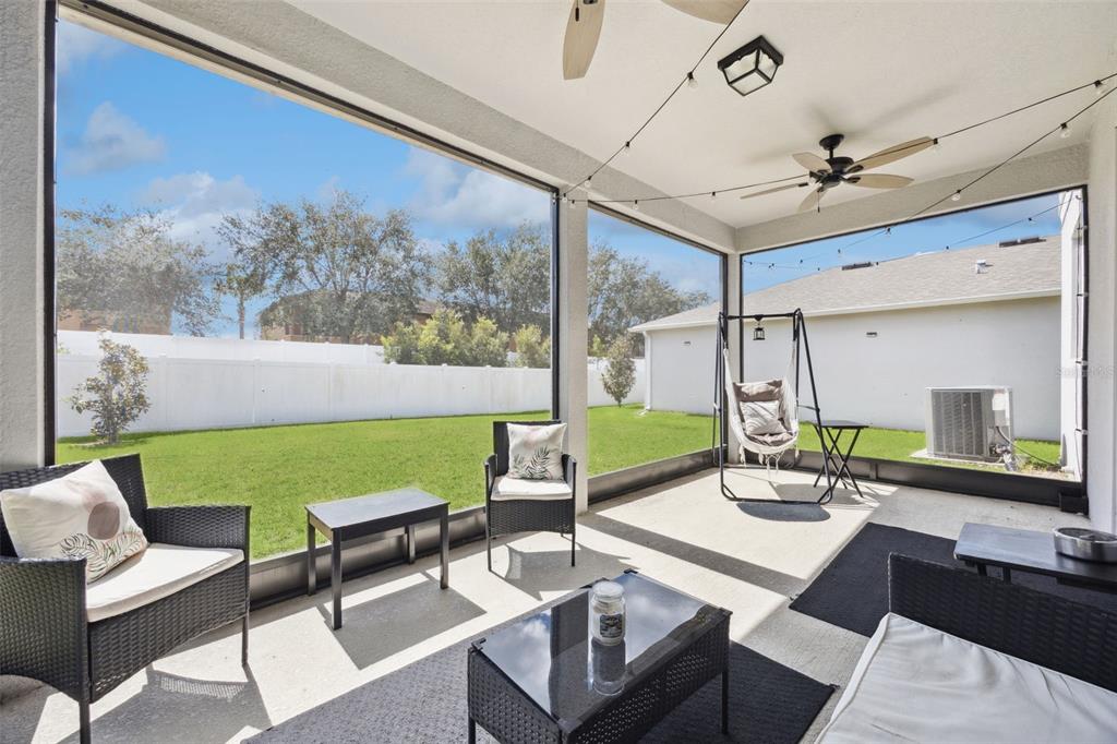 A screened-in patio features wicker furniture, a hanging chair, and a view of the backyard — 1068 PAPAYA CIRCLE, DAVENPORT, FL