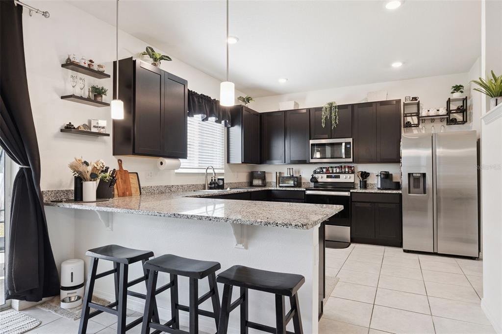 A kitchen features dark cabinets, granite countertops, stainless steel appliances, and a breakfast bar — 1068 PAPAYA CIRCLE, DAVENPORT, FL