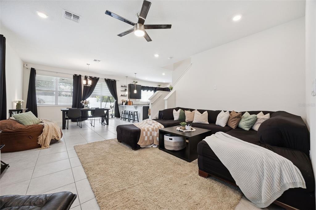 An open-concept living room features a large black sectional sofa, tile flooring, and dining area — 1068 PAPAYA CIRCLE, DAVENPORT, FL