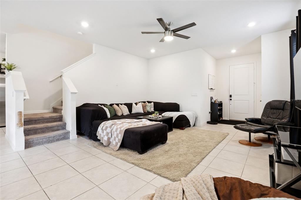 A living room features a black sectional sofa, a beige rug, and stairs with carpet — 1068 PAPAYA CIRCLE, DAVENPORT, FL
