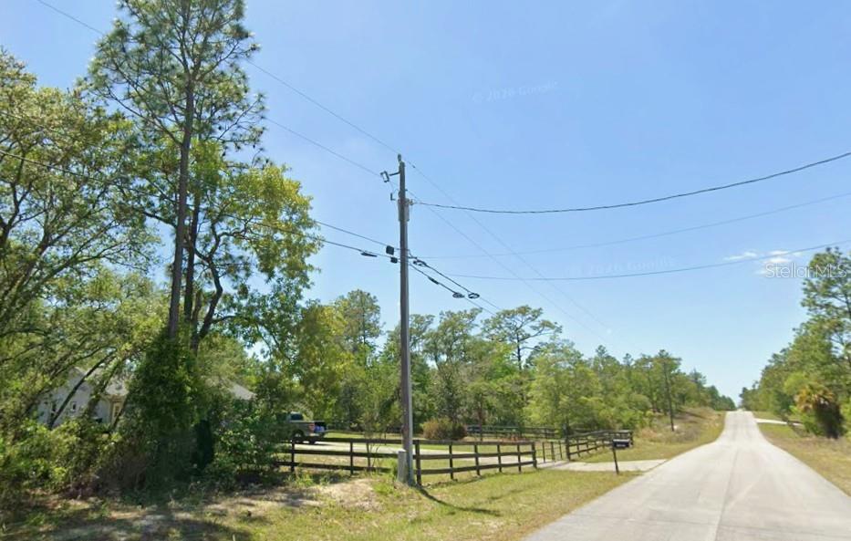 A utility pole stands beside a paved road near a fenced property with trees — SW NAUTILUS BOULEVARD, DUNNELLON, FL