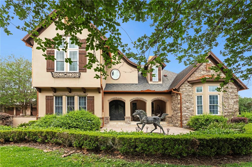 A two-story house with stucco and stone siding, a horse statue, and a paved courtyard — 11410 TROTTING DOWN DRIVE, ODESSA, FL