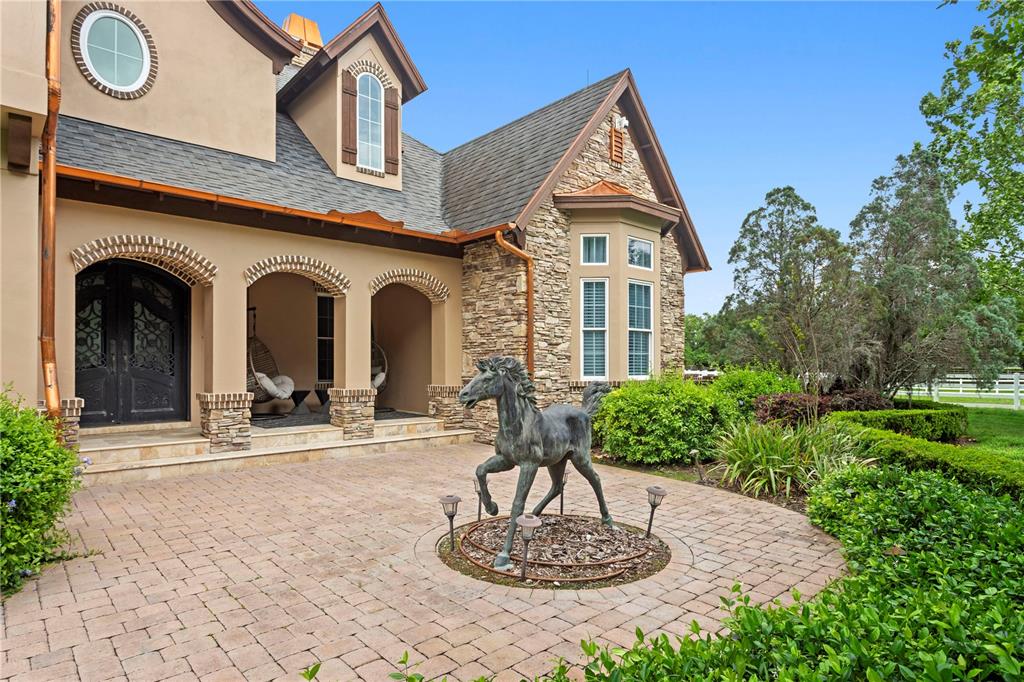 A stone and stucco house exterior features a brick patio with a bronze horse statue — 11410 TROTTING DOWN DRIVE, ODESSA, FL