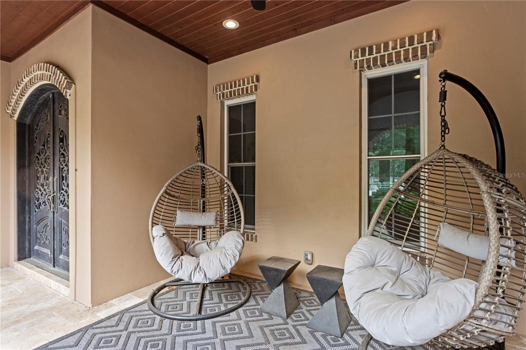 A covered patio features two hanging wicker chairs, a geometric rug, and arched doorways — 11410 TROTTING DOWN DRIVE, ODESSA, FL
