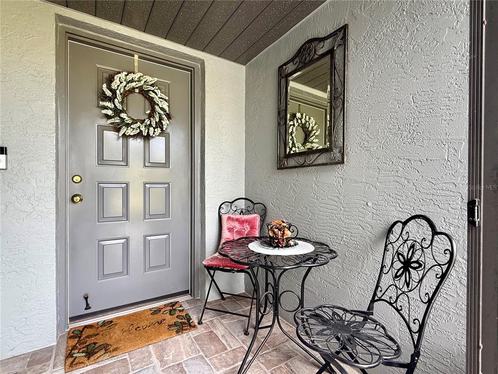 A gray front door with a wreath and a small bistro set on a porch — 1742 W ORANGEWOOD PLACE, AVON PARK, FL