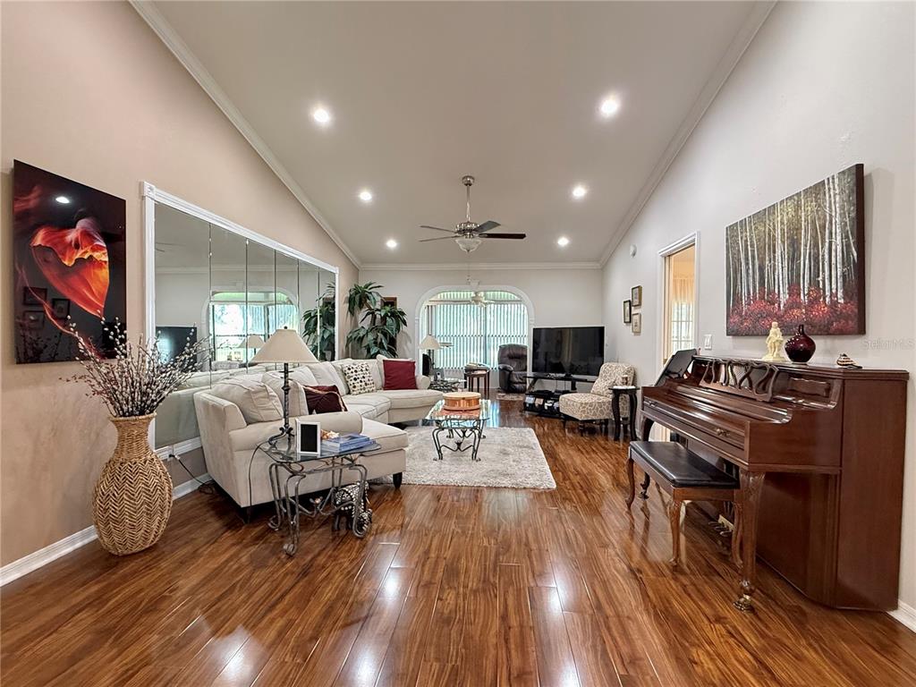 A living room features hardwood floors, a sectional sofa, a piano, and a mirrored wall — 1742 W ORANGEWOOD PLACE, AVON PARK, FL