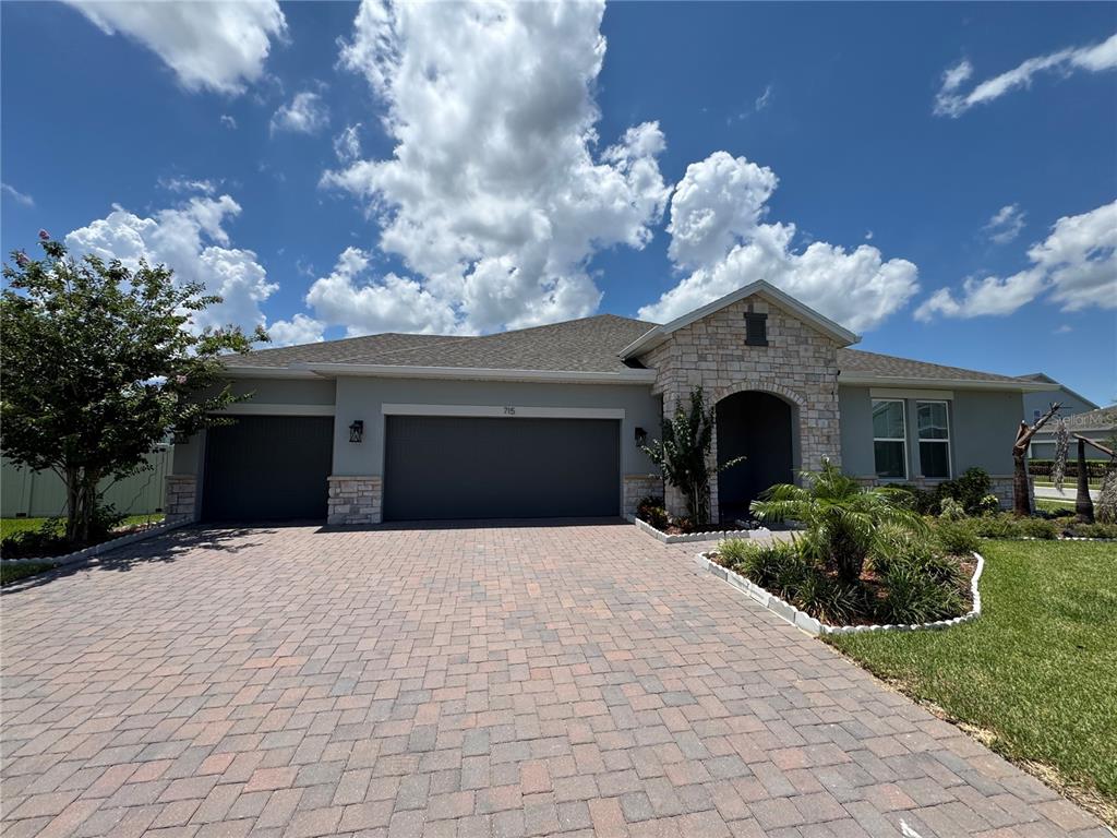 A single-story house with a stone-accented entryway, a paver driveway, and a three-car garage — 715 BLUE CITRUS LANE, MINNEOLA, FL