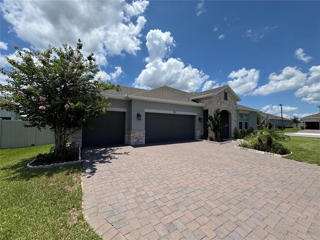 A single-story house with a stone facade, gray garage doors, and a brick paver driveway — 715 BLUE CITRUS LANE, MINNEOLA, FL
