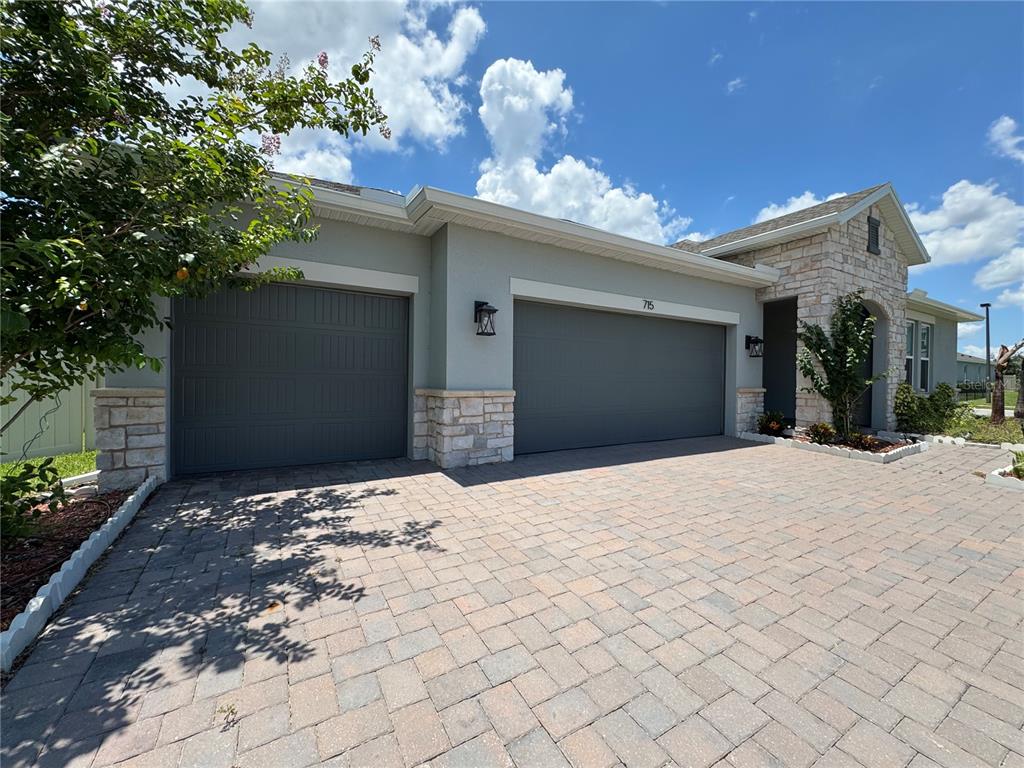 A house exterior features a three-car garage, stone accents, and a paved driveway — 715 BLUE CITRUS LANE, MINNEOLA, FL