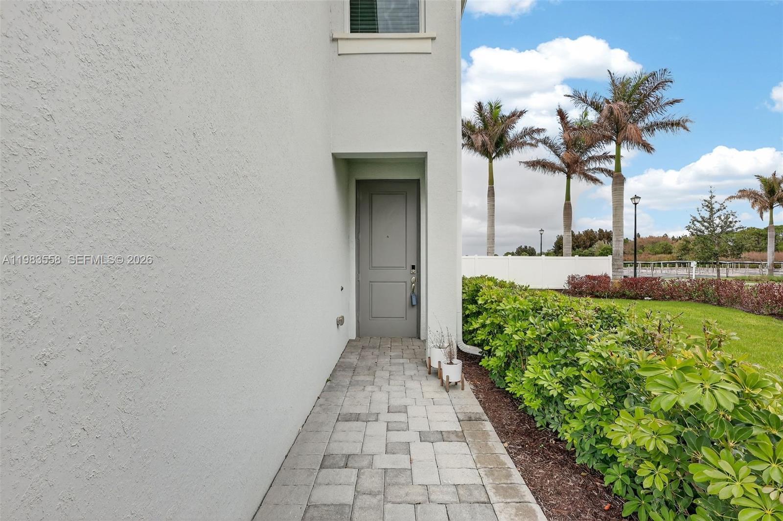 A paved walkway leads to a gray front door beside a hedge and palm trees — 5610 SE Edgewater Cir, Stuart FL 34997, STUART, FL