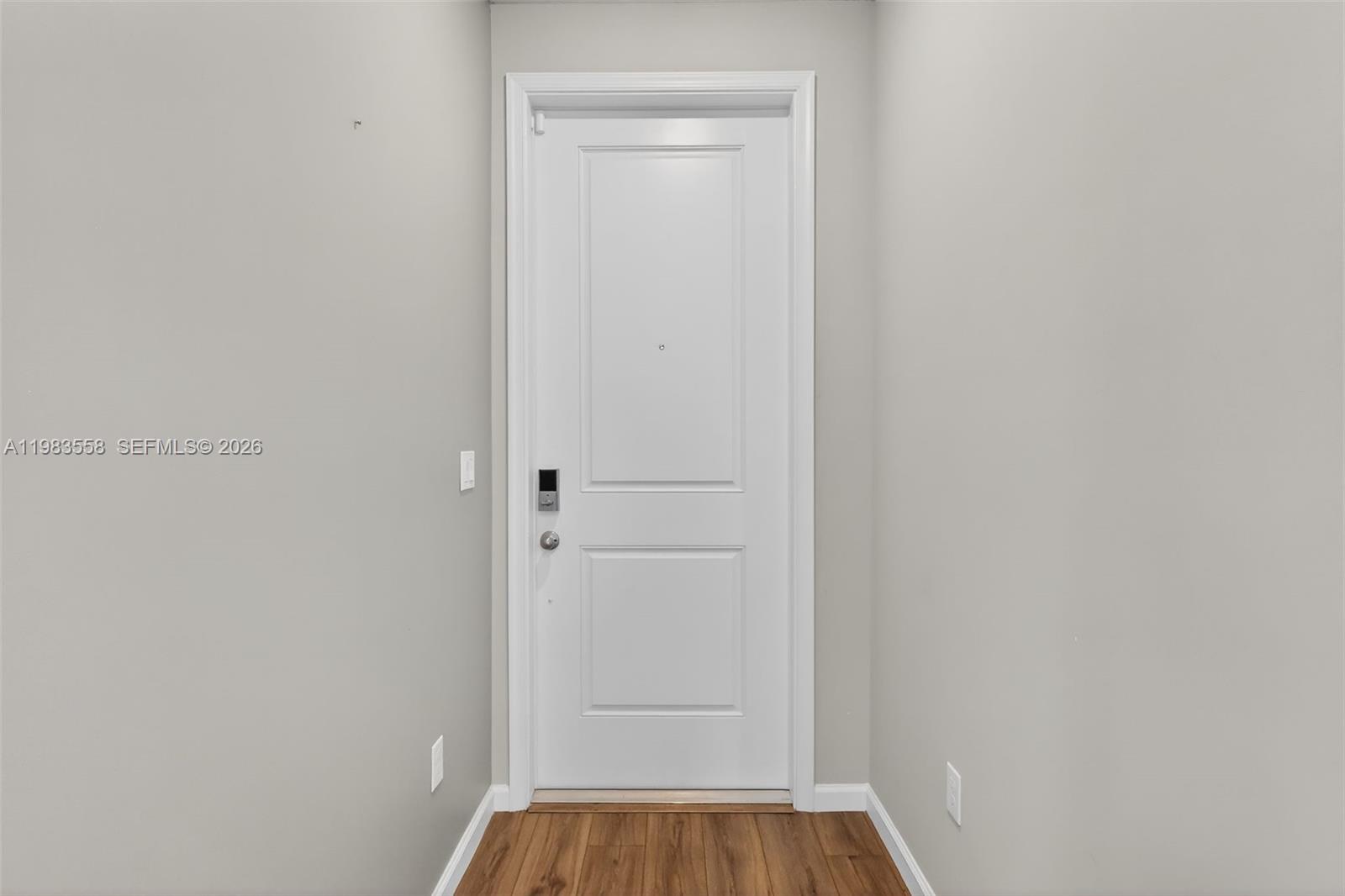 A white door with a smart lock is centered in a hallway with wood flooring — 5610 SE Edgewater Cir, Stuart FL 34997, STUART, FL