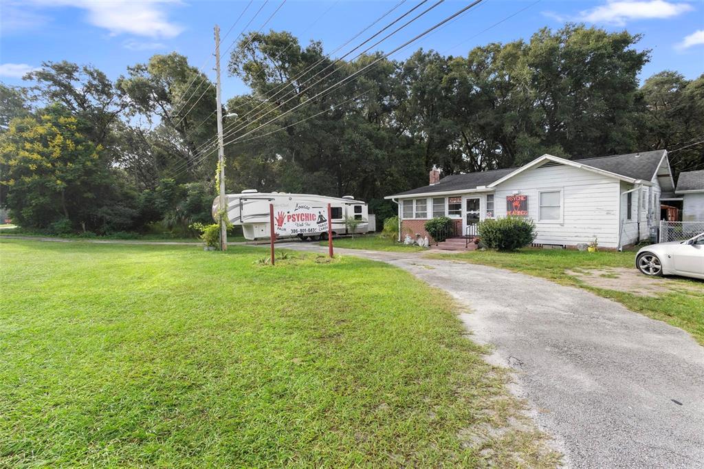 A white house with a driveway, a psychic sign, and a parked RV in the yard — 2480 N WOODLAND BOULEVARD, DELAND, FL