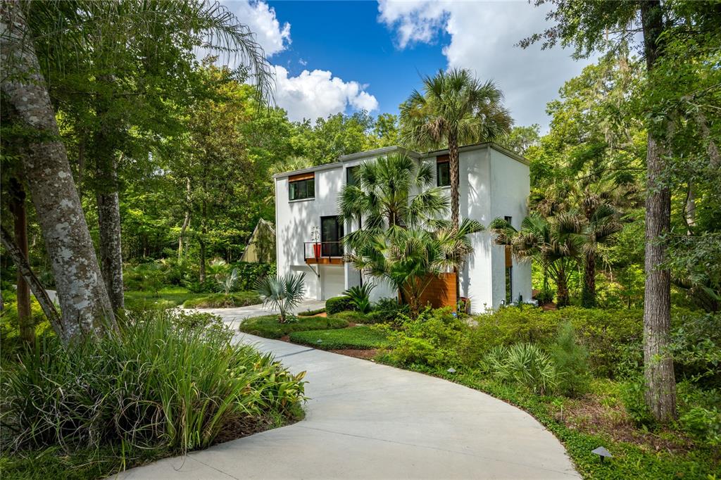 A modern white two-story house sits at the end of a concrete driveway among trees — 2012 NW 24TH STREET, GAINESVILLE, FL