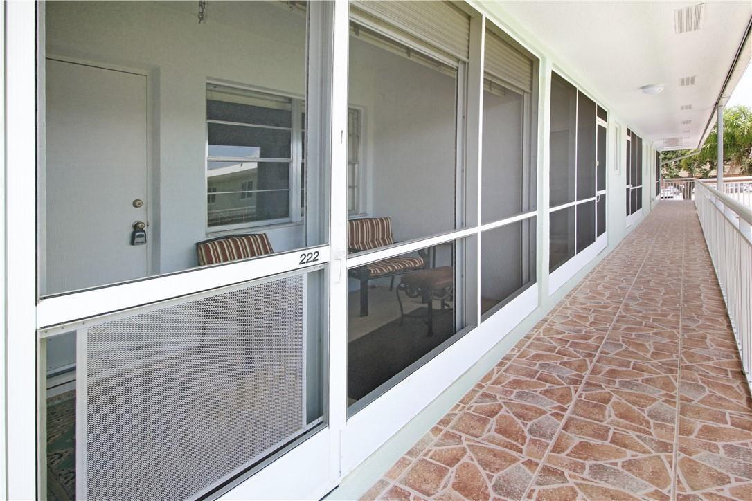 A tiled outdoor walkway leads past screened-in porches with sliding glass doors and unit number 222 — 2100 NE 38th Street # 222, Lighthouse Point FL 33064, LIGHTHOUSE POINT, FL