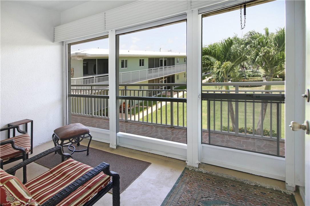 A screened-in balcony with outdoor furniture overlooks a grassy courtyard and a neighboring apartment building — 2100 NE 38th Street # 222, Lighthouse Point FL 33064, LIGHTHOUSE POINT, FL