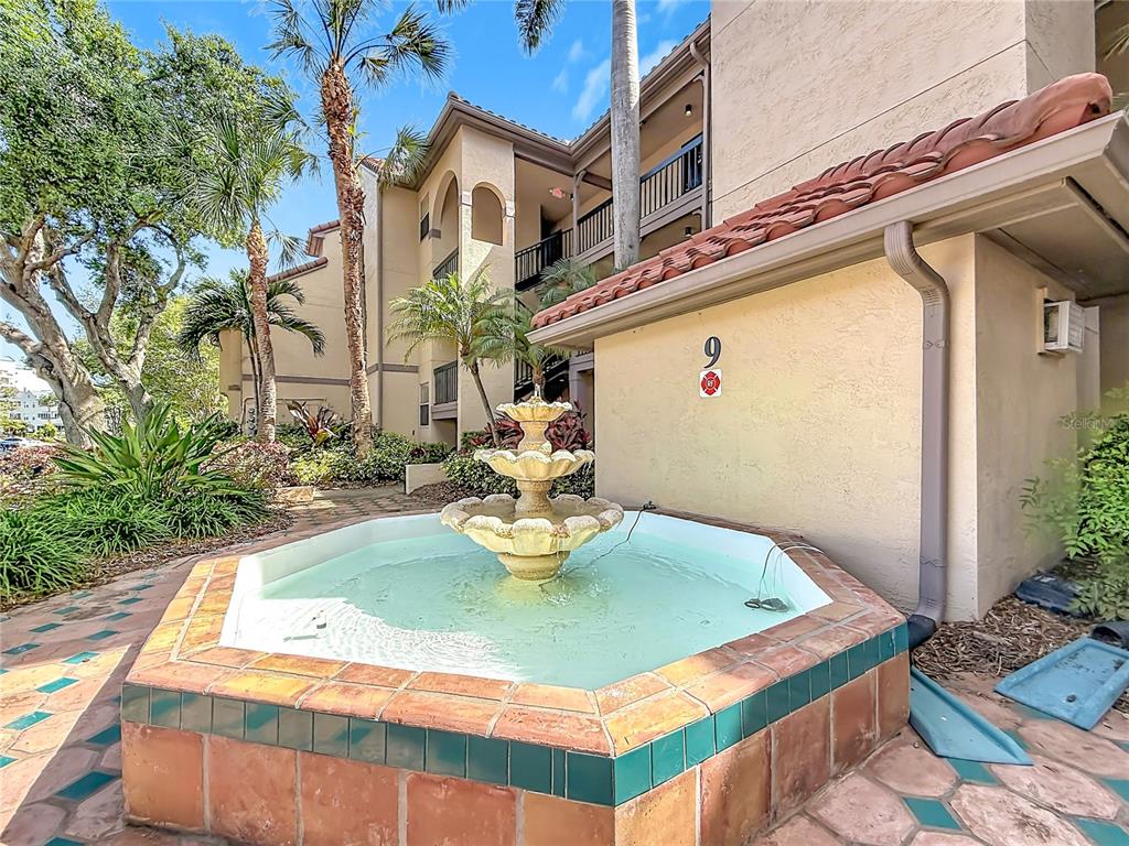 A three-tiered stone fountain sits in front of a multi-story tan stucco apartment building — 2400 FEATHER SOUND DRIVE UNIT 933, CLEARWATER, FL