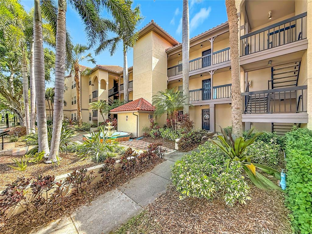 A multi-story apartment building features exterior staircases, palm trees, and a small fountain — 2400 FEATHER SOUND DRIVE UNIT 933, CLEARWATER, FL