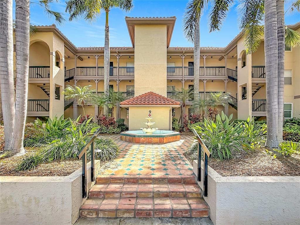 A multi-story apartment building exterior features a central fountain, tiled steps, and palm trees — 2400 FEATHER SOUND DRIVE UNIT 933, CLEARWATER, FL