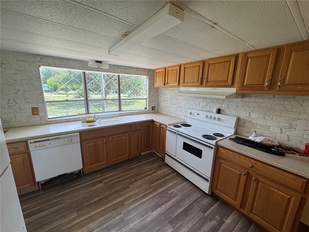 A kitchen features wood cabinets, white appliances, a tiled backsplash, and a large window — 11351 S ANN POINT, HOMOSASSA, FL
